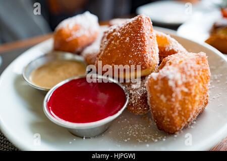 Nahaufnahme von Beignet Donuts mit Himbeer-DIP-Sauce auf einem weißen Teller, bestreut mit Puderzucker, San Francisco, Kalifornien, 22. Januar 2017. Stockfoto