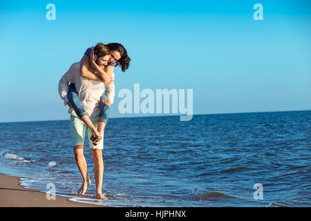 Handsome man geben Huckepack zu seiner Freundin am Strand Stockfoto