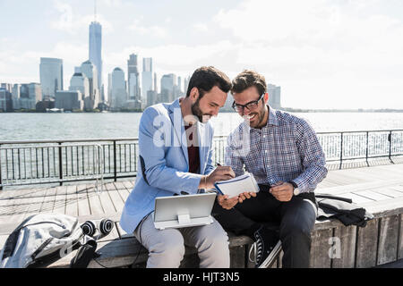 USA, zwei Geschäftsleute arbeiten bei New Jersey am Wasser mit Blick auf Manhattan Stockfoto