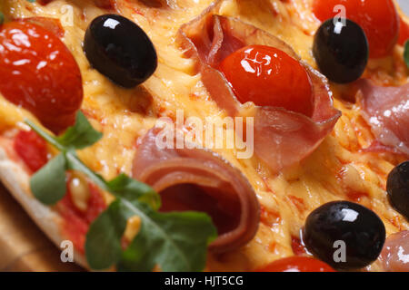 Italienische Pizza mit Schinken, Tomaten, schwarzen Oliven und Rucola horizontale Makro Textur Stockfoto