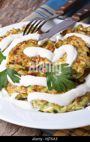 Zucchini-Pfannkuchen mit Sauerrahm Closeup auf einem weißen Teller auf den Tisch, die vertikale Stockfoto
