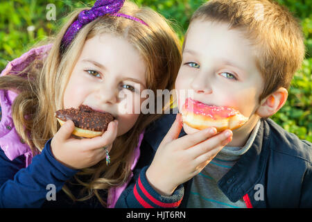 glückliche Kinder essen Donuts sitzen auf dem grünen Rasen im park Stockfoto