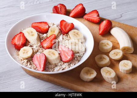 Müsli mit frischen Erdbeeren und Bananen mit gehackten Zutaten Closeup auf einem Holztisch. horizontale Stockfoto