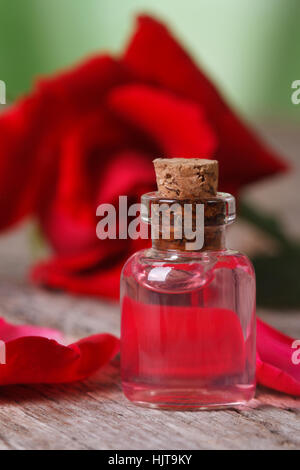 Rosenöl in einer Flasche auf einem Hintergrund von roten Rosen. vertikale Makro Stockfoto