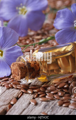 Leinsamen, blaue Blumen und Öl in der Flasche-Makro auf vertikalen hölzernen Hintergrund Stockfoto