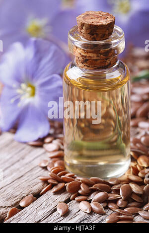 Leinöl in einem Glas Flasche Makro auf einem Hintergrund von Blüten und Samen vertikale Stockfoto