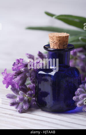 Lavendelöl in einer blauen Glasflasche und Blumen auf dem Tisch. vertikale Makro Stockfoto
