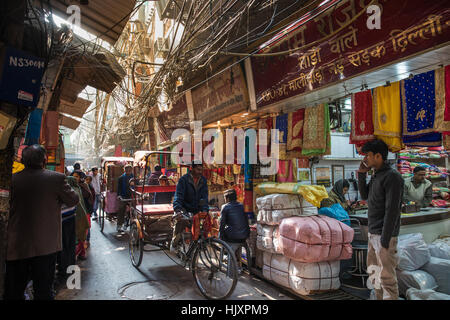 Zyklus Rikschafahrer übergeben einen Sari Shop auf einer belebten und schmalen Gasse in berühmten Chandni Chowk-Markt von Neu-Delhi, Indien. Stockfoto