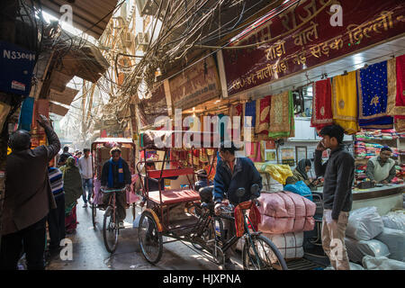 Zyklus Rikschafahrer übergeben einen Sari Shop auf einer belebten und schmalen Gasse in berühmten Chandni Chowk-Markt von Neu-Delhi, Indien. Stockfoto