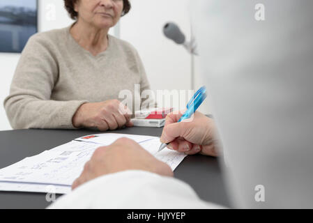 Arzt, der sich mit einer leitenden Patientin und einem Kardiologen bekonsultiert, um die EKG-Ergebnisse zu erklären und Medikamente zu verordnen. Stockfoto