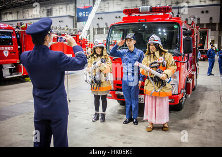 Feuerwehrmann unter Bild von zwei Mädchen verkleidet als Feuerwehrmänner mit einem Feuerwehrmann, während Dezomeshiki oder Neujahr Parade von Tokyo Fire Department Stockfoto