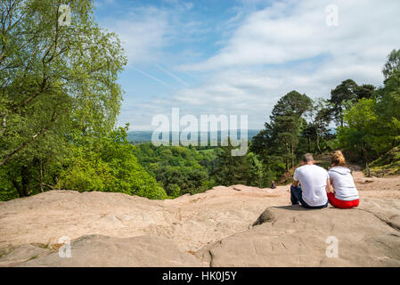 Junges Paar saß auf den Felsen an einem stürmischen Punkt, Alderley Edge. Ein bekannter Aussichtspunkt in die Landschaft von Cheshire. Stockfoto
