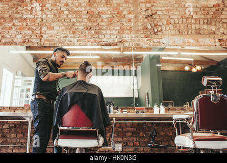 Stilvolle Friseur Haarschnitt an Kunden in seinem Geschäft zu geben. Friseur Haare schneiden der Mann sitzt im Stuhl im Salon. Stockfoto