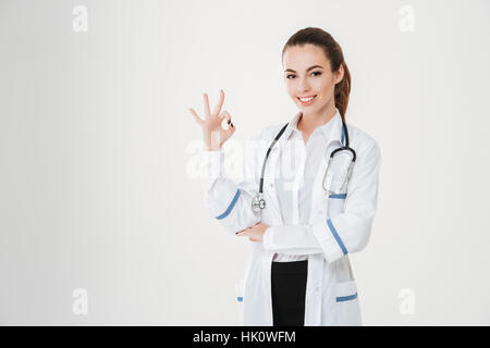 Lächelnde schöne junge Frau Doktor zeigt ok Geste auf weißem Hintergrund Stockfoto