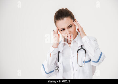 Traurig betonte junge Ärztin, die Kopfschmerzen über weißem Hintergrund Stockfoto