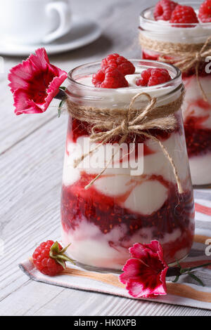 frische Himbeeren Joghurt in ein Glas-Glas-Nahaufnahme auf einem Tisch mit Blumen geschmückt. vertikale Stockfoto