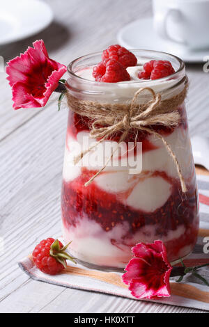 Milch-Dessert mit frischen Himbeeren in einer Glas-Glas-Nahaufnahme dekoriert mit Blumen auf einem Holztisch. vertikale Stockfoto