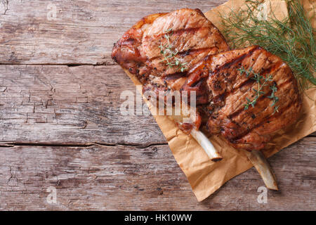 zwei Stücke von gegrilltem Schweinefleisch mit Kräutern auf ein Papier auf einem alten Tisch Draufsicht horizontale Nahaufnahme Stockfoto