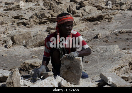 Der Ferne Mann hacken Salzblöcke mit einer Axt in der Wüste Danakil-Senke in Tigray, Äthiopien Stockfoto