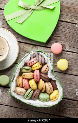 Bunte Macarons in Valentinstag herzförmigen Geschenk-Box und Kaffee Tasse auf Holztisch. Ansicht von oben Stockfoto