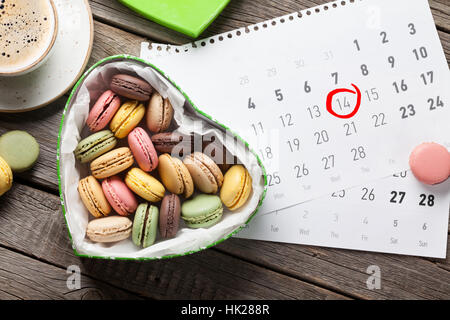 Valentinstag-Grußkarte. Makronen in Herzform Geschenk-Box und Kaffee Tasse über Februar Kalender. Ansicht von oben Stockfoto