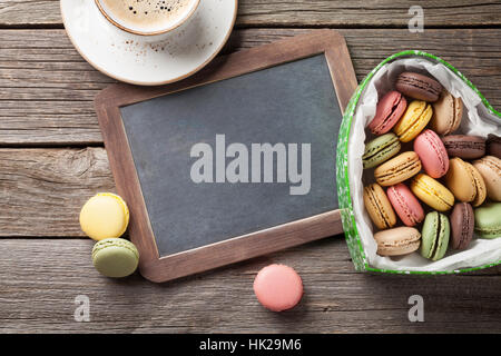 Bunte Macarons in Valentinstag herzförmigen Geschenk-Box und Kaffee Tasse auf Holztisch. Draufsicht mit Tafel für Ihre Grüße Stockfoto