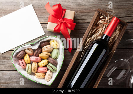 Valentinstag-Grußkarte. Rot Wein Geschenk Makronen Box und Gläser auf Holztisch. Draufsicht mit Platz für Ihre Grüße Stockfoto