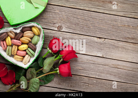 Valentinstag-Grußkarte. Rote Rosen und Makronen Geschenkbox auf Holztisch. Draufsicht mit Platz für Ihre Grüße Stockfoto