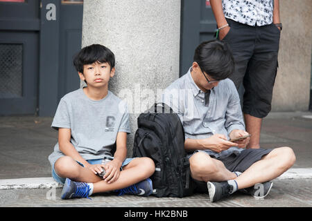 LONDON, ENGLAND - 12. Juli 2016 Vater und Sohn haben eine Pause auf dem Bürgersteig sitzen Stockfoto