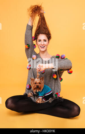 Porträt einer fröhlich lächelnde Frau mit roten Haaren, die Spaß mit ihrem Hund auf orangem Hintergrund isoliert Stockfoto