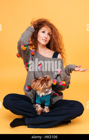 Porträt einer hübschen roten Haar-Frau mit textfreiraum auf ihrem Palm sitzend mit Hund isoliert auf orangem Hintergrund Stockfoto
