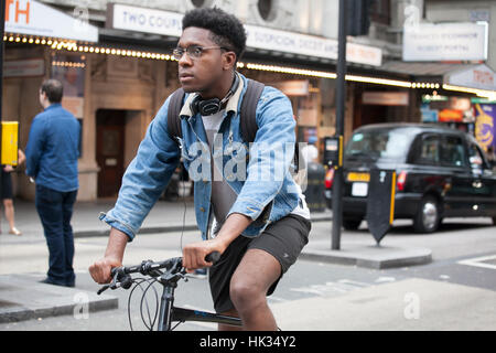 LONDON, ENGLAND - 12. Juli 2016 ernsten jungen Mann in einer Jeansjacke und kurze Shorts, die mit dem Fahrrad auf der Straße Stockfoto