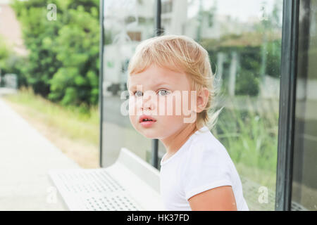 Close-up Portrait. Niedliche kaukasischen blonde Babymädchen wartet auf eine Bushaltestelle Stockfoto