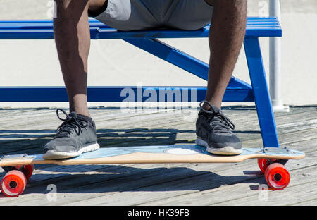 Männliche Füße auf Skateboard sitzend auf einer Bank Stockfoto