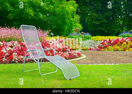 Liegestuhl im Park neben dem Blumenbeet Stockfoto