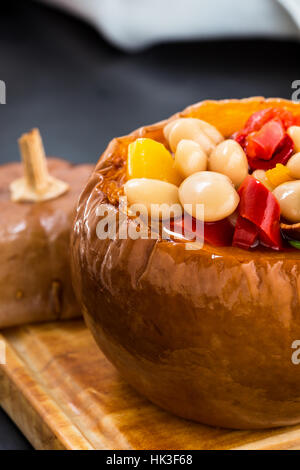 Weiße Bohnen und Paprika-Gemüse-Eintopf in Kürbis Schüsseln serviert auf Holzbrett Stockfoto