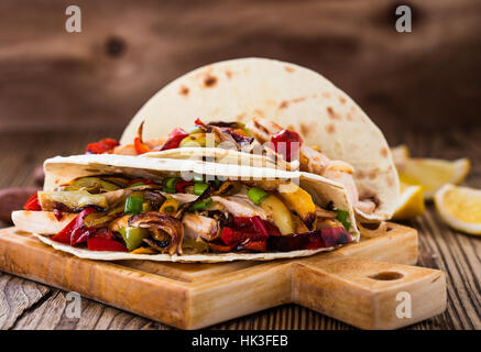 Chicken Sie Fajitas mit gegrillten Zwiebeln und Paprika und mit Mehltortillas auf ländlichen Holzbrett servieren Stockfoto