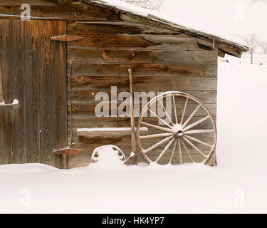 Verwitterte Holzschuppen mit Wagenräder und Schnee - Platz, leichter Schneefall Stockfoto