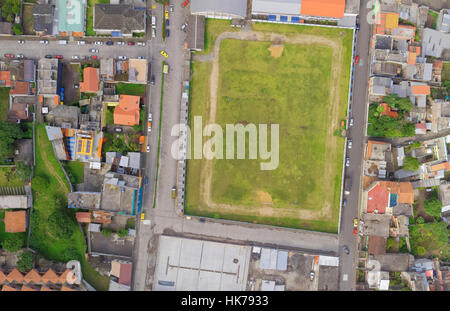 Ein Luftbild über der Decke erfasst ein großes rechteckiges Grasfeld, das von asphaltierten Straßen und dichten städtischen Wohngebäuden begrenzt wird. Das Feld, das Flecken von abgenutztem Gras und Schmutz zeigt, ist von einem umgeben Stockfoto