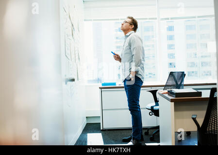 Ein Mann, der in einem Büro Blick auf Zettel angeheftet auf einem Whiteboard. Stockfoto