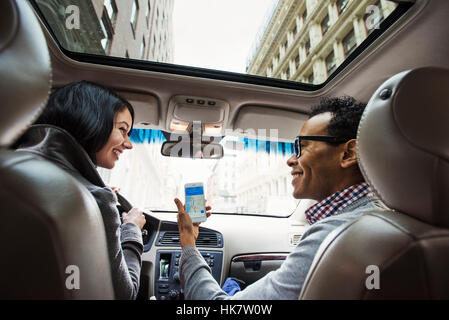Eine junge Frau und ein junger Mann in einem Auto Blick auf eine Karte auf dem Display eines Handys, gesehen von der Rückbank. Stockfoto