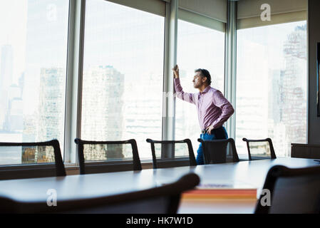 Ein Mann in einem Konferenzraum Blick aus dem Fenster auf eine Stadtlandschaft. Stockfoto