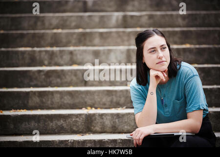 Eine junge Frau sitzt auf einer Treppe mit einem geschlossenen Laptop auf den Knien. Stockfoto