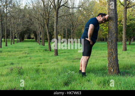 Abstrakt und konzeptionelle müde, müde Mann im Wald. Mann niedergedrückt, ruhen Sie sich nach einem Lauf in den Wald, an einen Baum gelehnt. Stockfoto