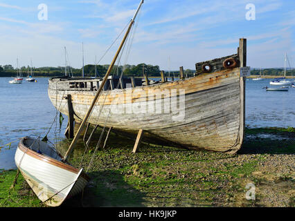 Alter, reparaturbedürftige Bootsrumpf zum Verkauf neben einem Segeljolle bei Ebbe am Dell Quay, in Chichester Harbour, West Sussex, England, Großbritannien Stockfoto