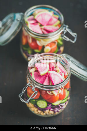 Gesundes Mittagessen zum Mitnehmen-Gläser. Gemüse und Kichererbsen sprießen geschichteten vegane Salat in Gläsern über verbrannten Holz dunkel, selektiven Fokus. C Stockfoto