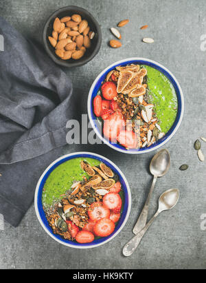 Gesundes Frühstück. Grüner Smoothie Schalen mit Erdbeeren, Müsli, Chia und Kürbis-Samen, getrocknete Feigen und Mandeln über graue konkreten Hintergrund, top Stockfoto