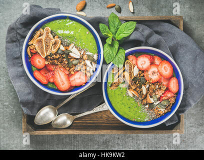 Gesundes Frühstück. Grüner Smoothie Schalen mit Erdbeeren, Müsli, Chia und Kürbis-Samen, getrocknete Feigen und Mutter in Holztablett über grauen Beton backg Stockfoto