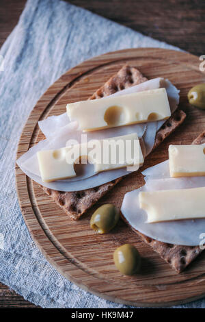 Schinken und Käse Knäckebrot Sandwiches und Oliven serviert auf einem Holzbrett Stockfoto