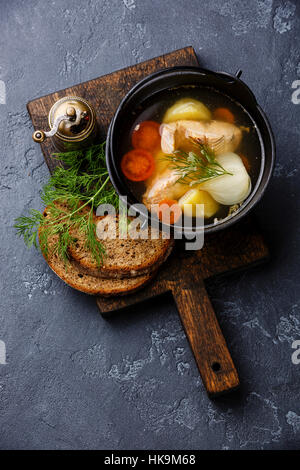 Fischsuppe mit Lachs, Kartoffeln und Karotten in schwarzem Eisentopf auf dunklem Stein Stockfoto